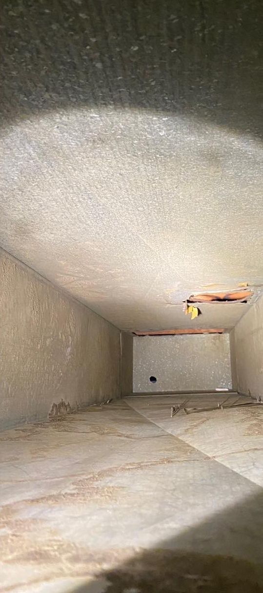 Interior view of a rectangular duct, light coming from top, walls are textured, visible dust and debris.