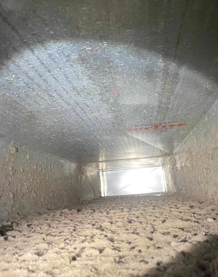 Inside of a dusty HVAC duct. The metal walls are covered in a thick layer of debris, viewed from inside the duct.