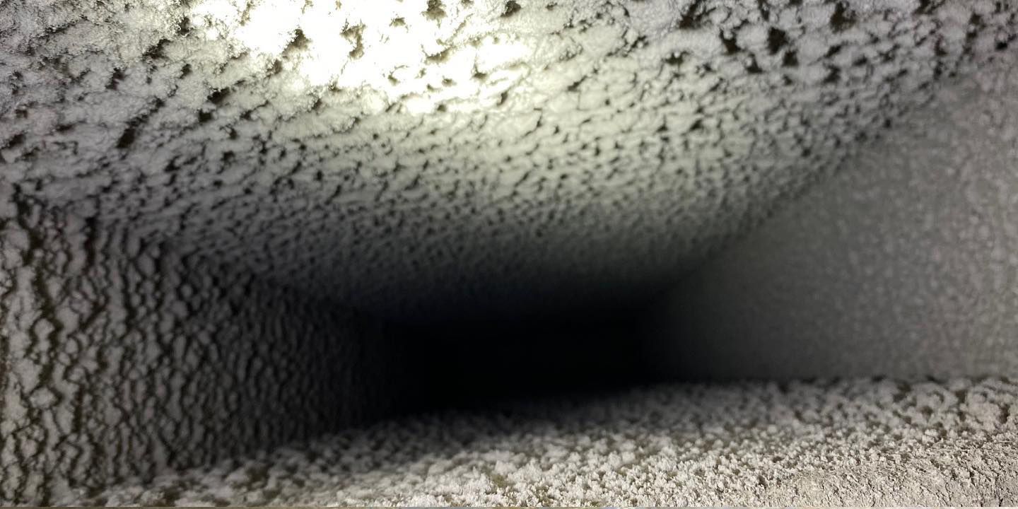 A close-up view inside a dusty, square air duct with light shining from the entrance.