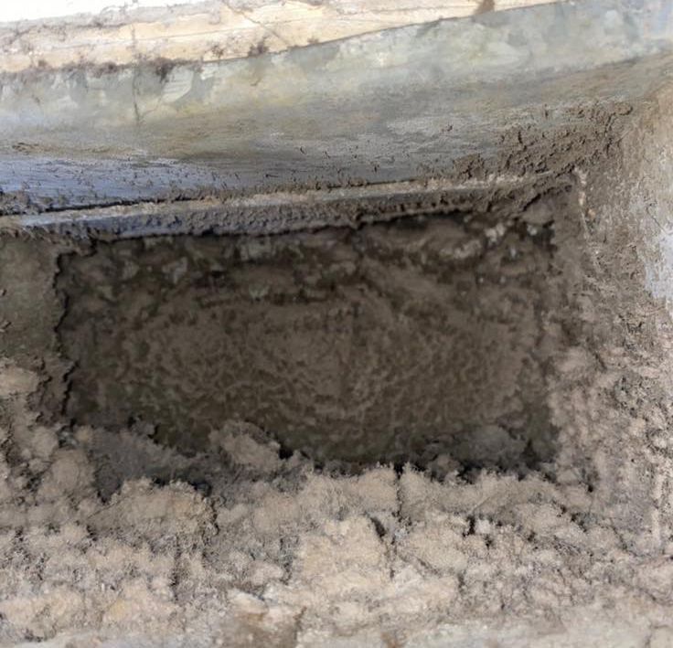 Dust-filled air vent, gray concrete frame. The opening is coated in thick, matted dust.