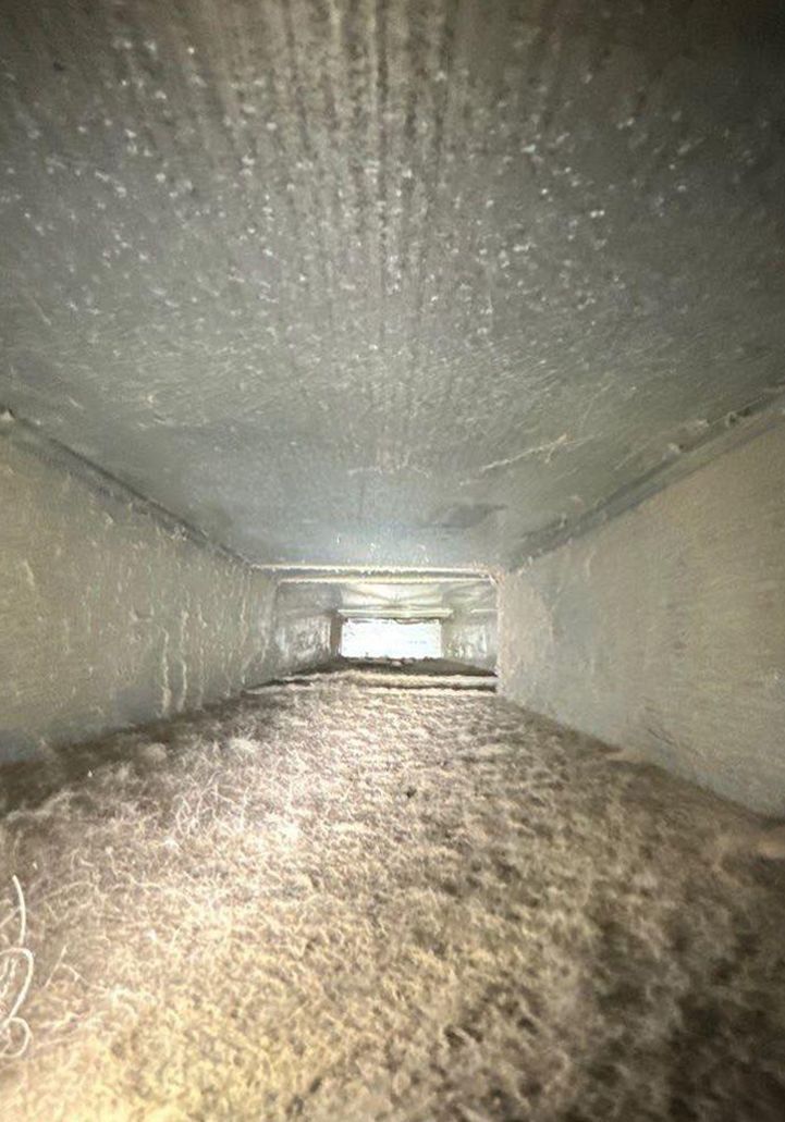 Dirty air duct interior, filled with dust and debris. Light shines at the end of the duct.