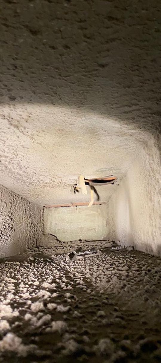 Inside a dusty, rectangular duct, looking upward. Some debris and a wire are visible.