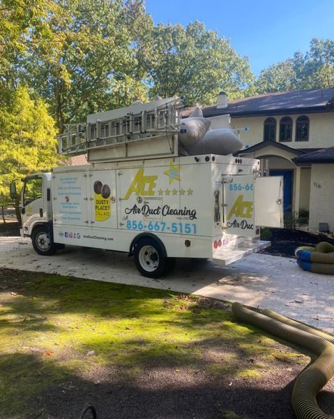 A white air duct cleaning truck parked in front of a house, with a ladder and hoses.