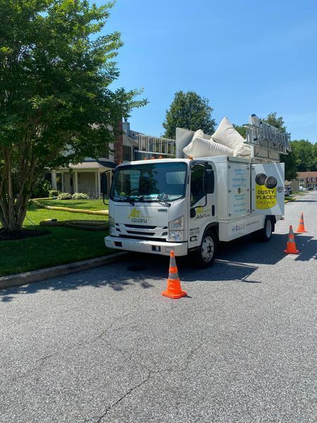 White utility truck with an extended boom parked on a street. Traffic cones surround the front. Sunny day.