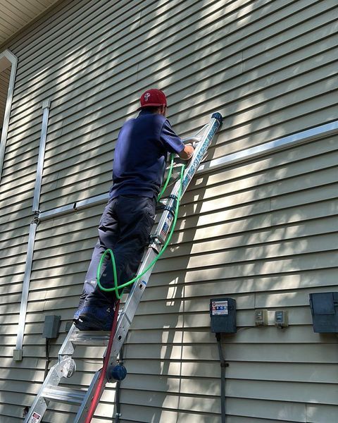 Person in red hard hat on ladder, working on the side of a house; green cable visible.