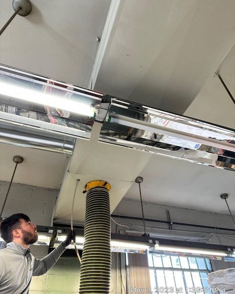 Man looking up at industrial lights and a vent system in a workshop.
