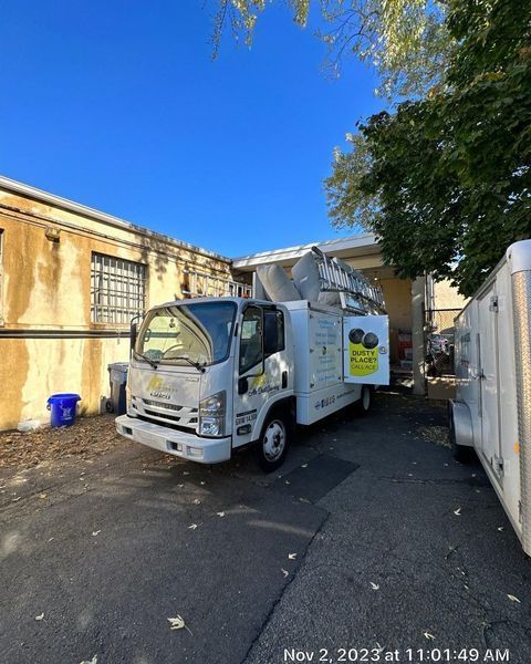 White utility truck parked next to a building, ladder extended towards a roof.
