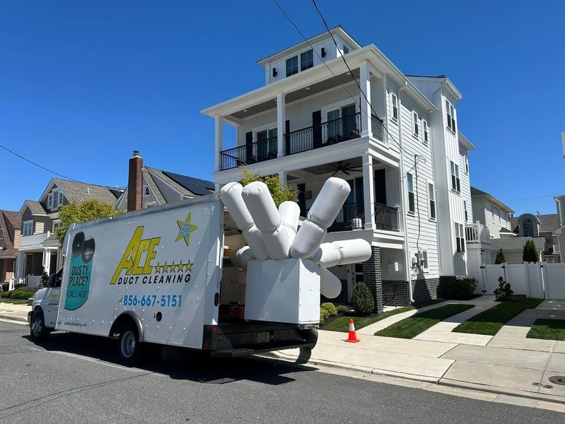 White cleaning truck parked in front of a white multi-story house on a sunny day.