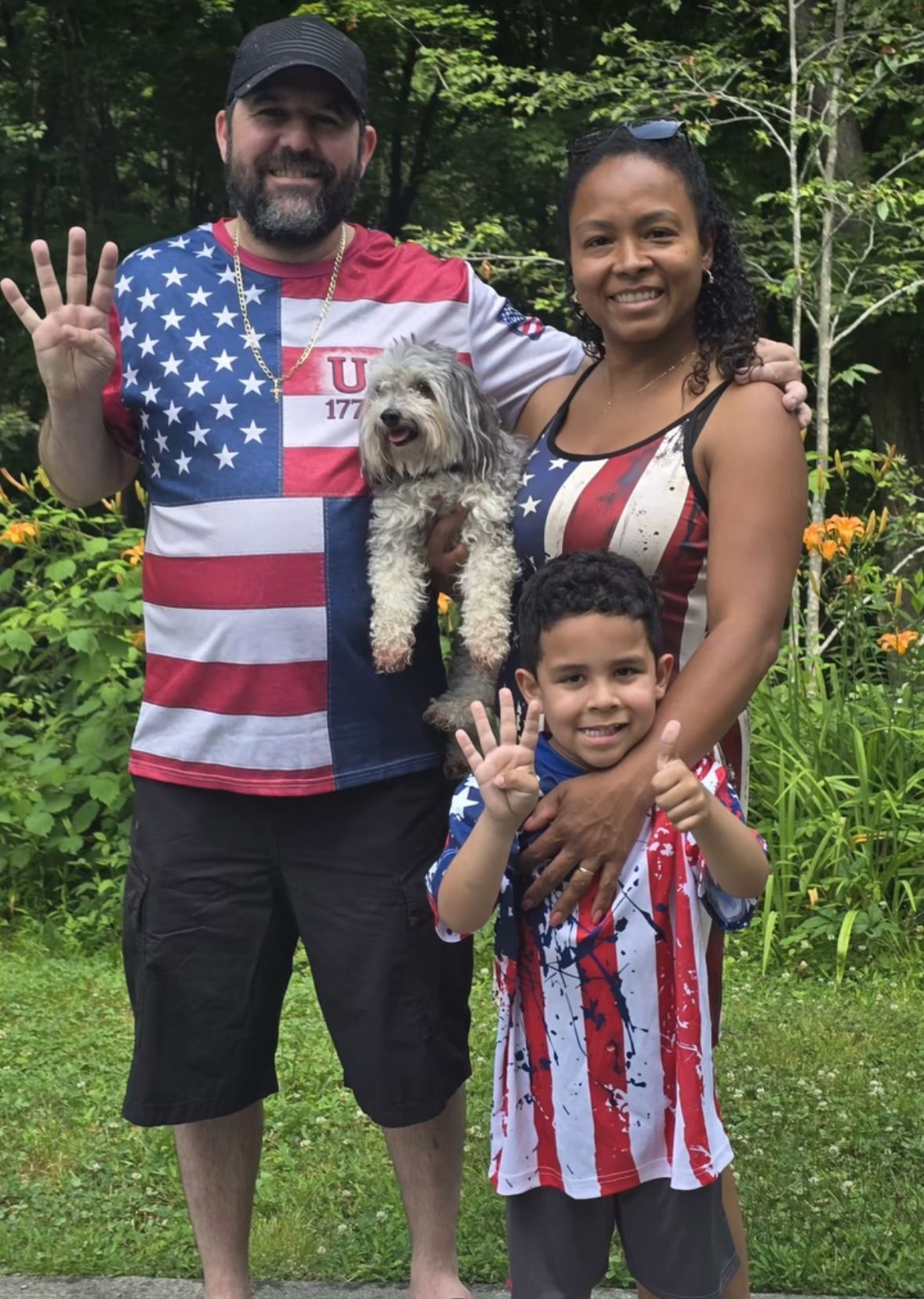 Family posing outdoors, holding a caught fish and wearing red, white, and blue shirts.