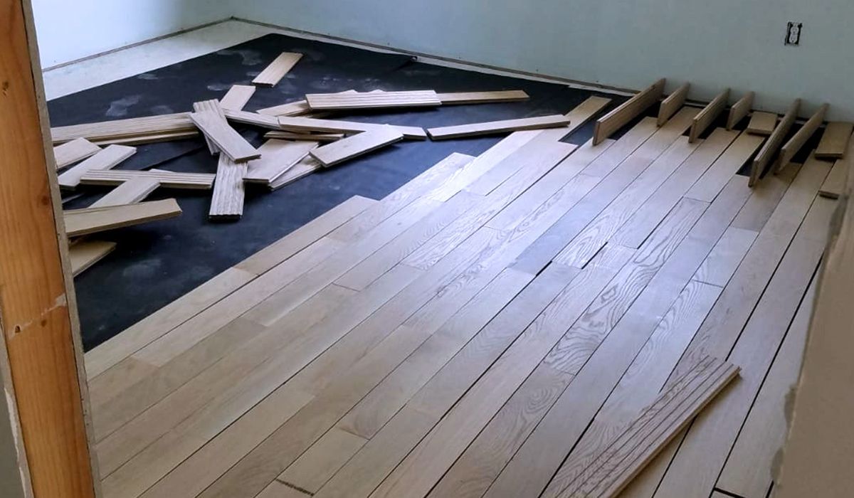 Damaged hardwood floor with broken boards and exposed subfloor in a room under repair