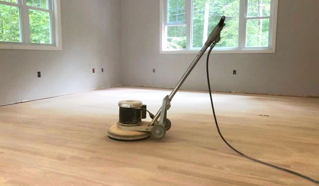 Floor sander in an empty room with hardwood floors and large windows