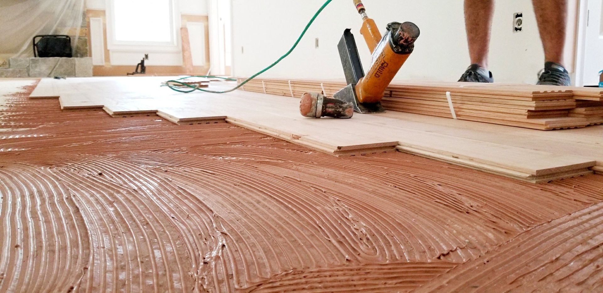 Person spreading adhesive with a trowel during a hardwood floor installation