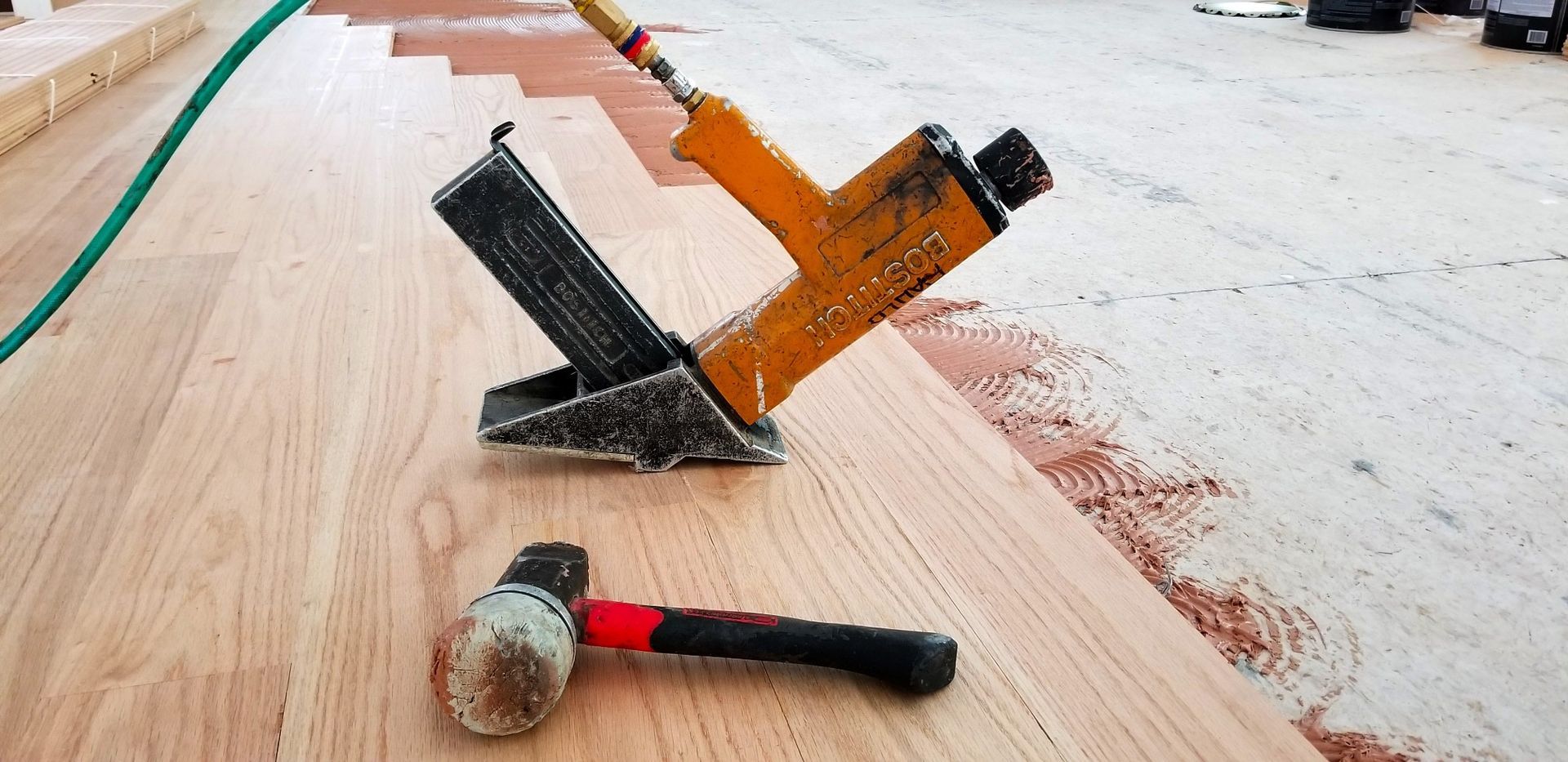 Construction tools on a wooden floor: a red hammer and two angled trowels with drywall dust.
