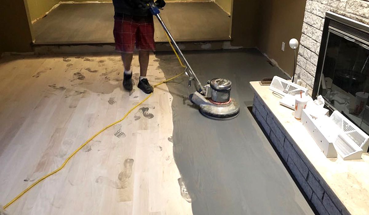 Person sanding a floor with a floor buffer in a room with exposed wood and a fireplace.