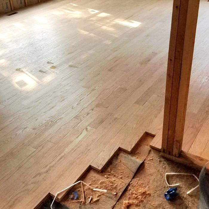 Freshly finished light wood floor with visible stair edge and construction debris at the bottom.