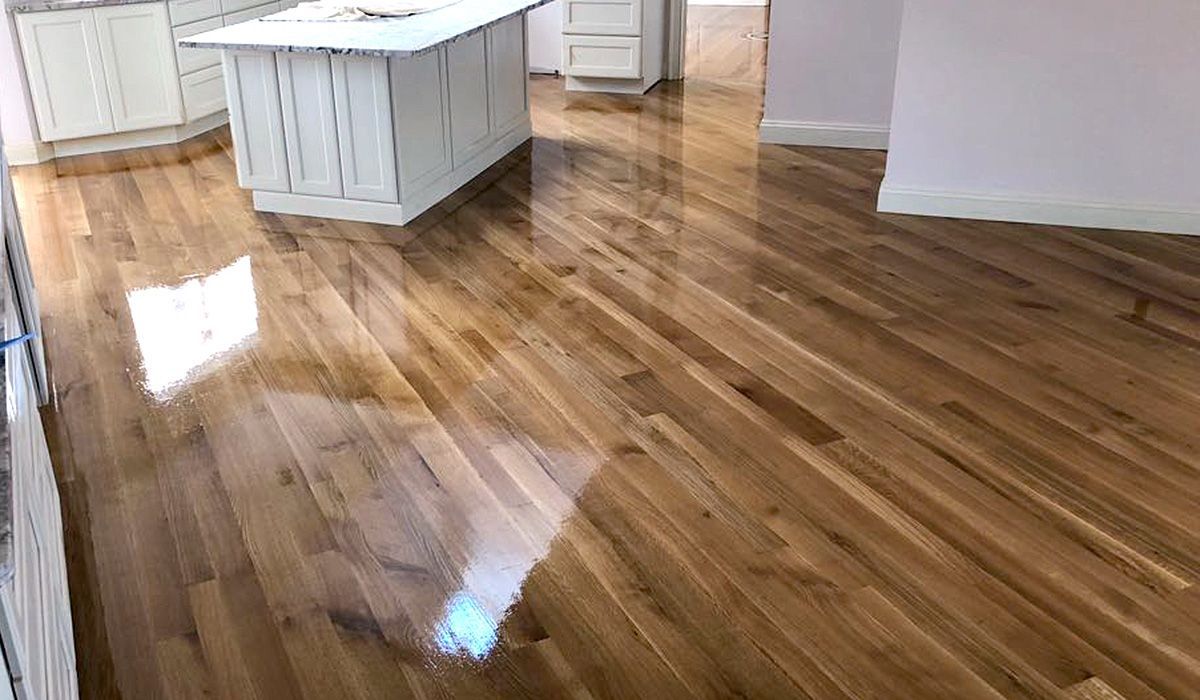 Polished hardwood floor in an empty kitchen with white cabinets and island, reflecting light