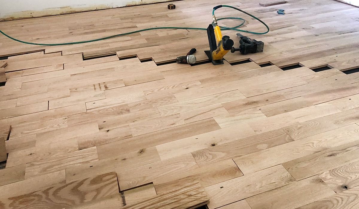 Wooden floorboards being installed, with a yellow power saw on unfinished flooring.