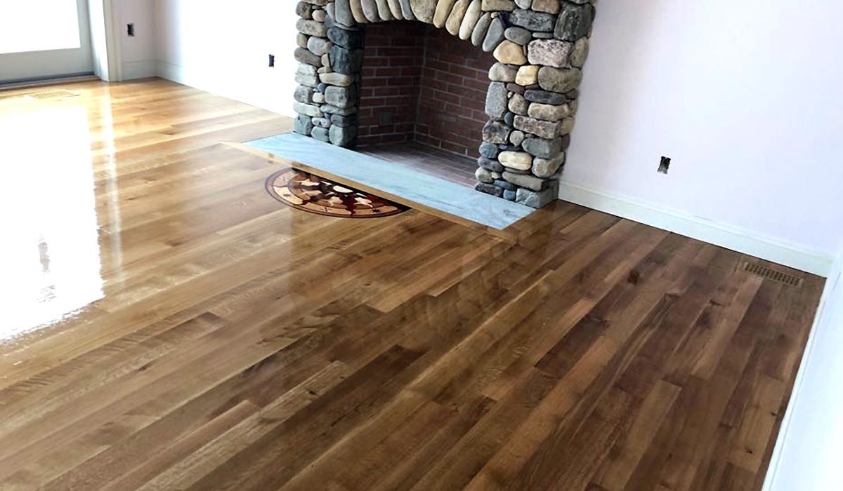 Empty living room with hardwood floors and a stone fireplace.