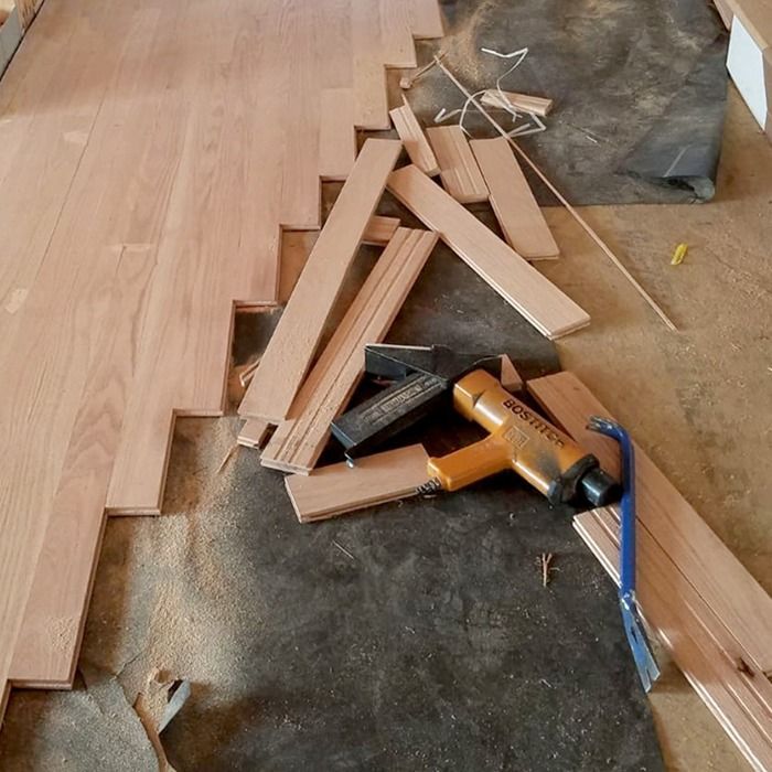 Loose wooden boards, a tape measure, and a power tool scattered on a partially installed floor.