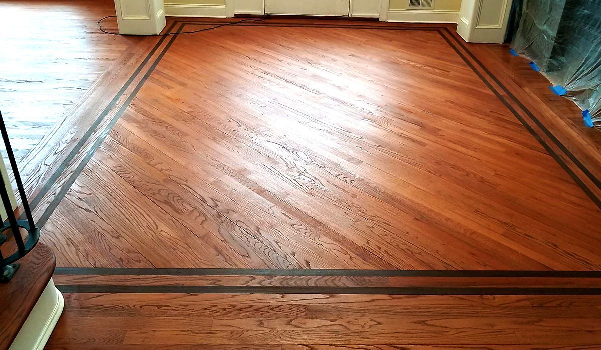Hardwood floor with a warm wood finish in a room, bordered by dark trim and curtains