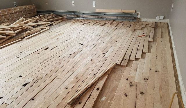 Wooden floorboards stacked and spread across a room during flooring installation.