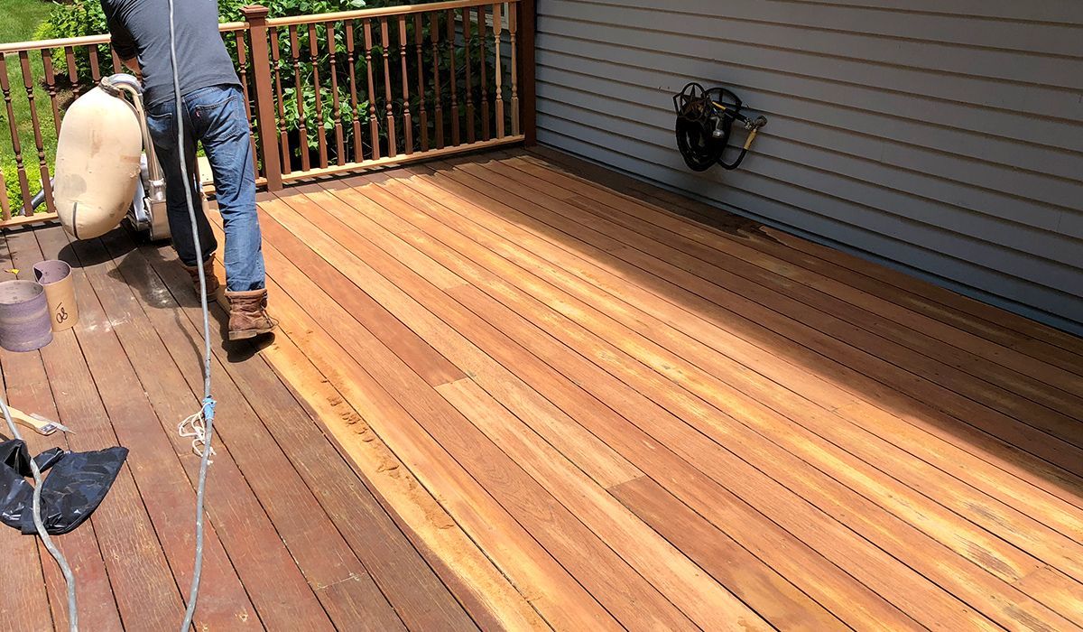 Person power-washing a wooden deck beside a house and railing