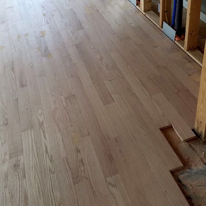 Light wood flooring under construction in a room, with exposed framing along the right edge.