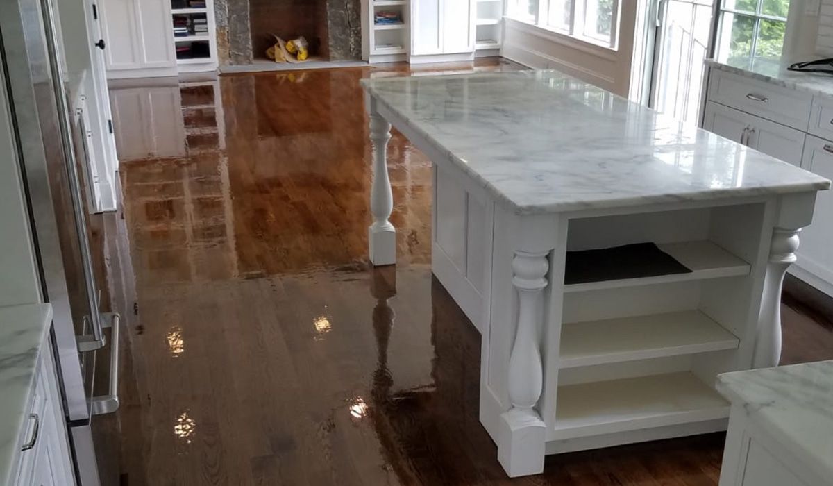 Bright kitchen with polished hardwood floors, white island, and large windows along the wall.