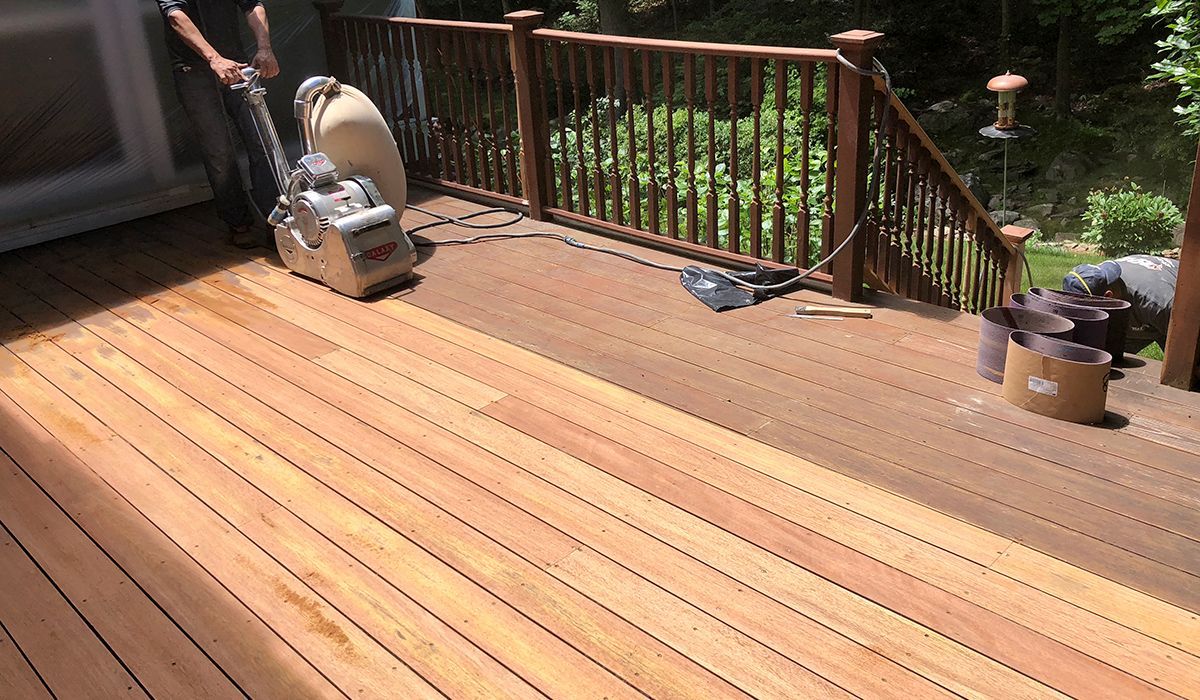 Wooden deck with railings, a lawn chair, and a grill in a sunlit backyard.