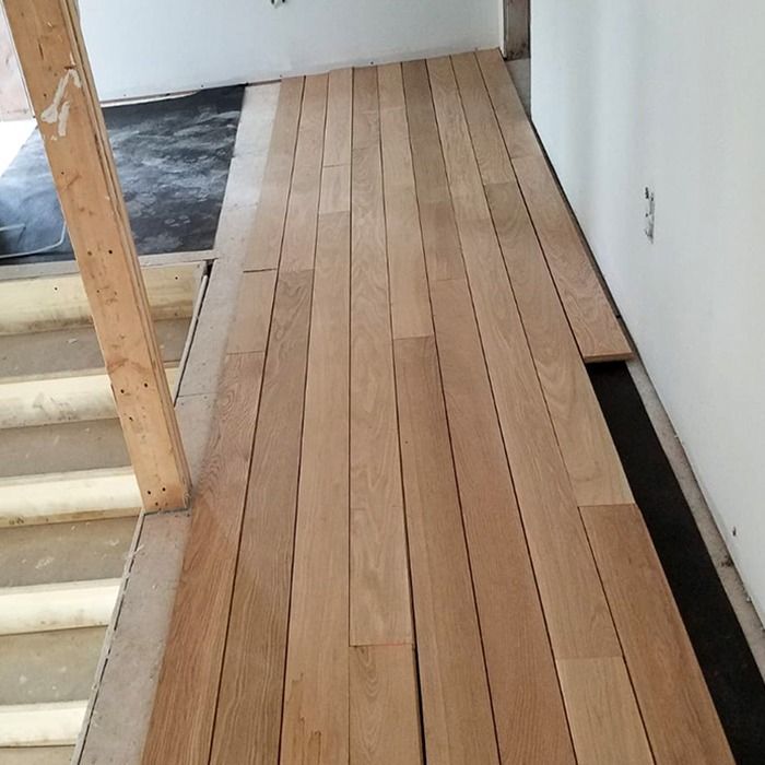 Partially installed light wood floorboards in a hallway under renovation