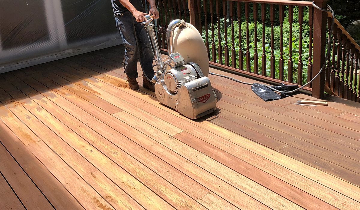 Person using a floor sander on a wooden deck in sunlight