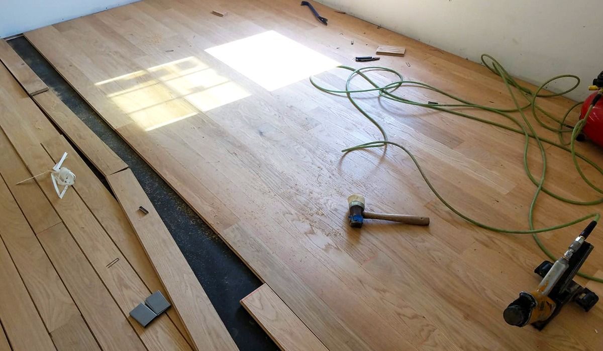 Partially installed hardwood floor with tools, cords, and a bright patch of sunlight on the boards.