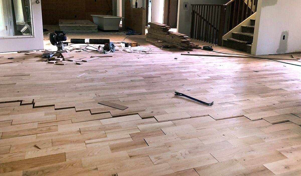 Partially installed hardwood flooring in a room with tools and debris near a doorway