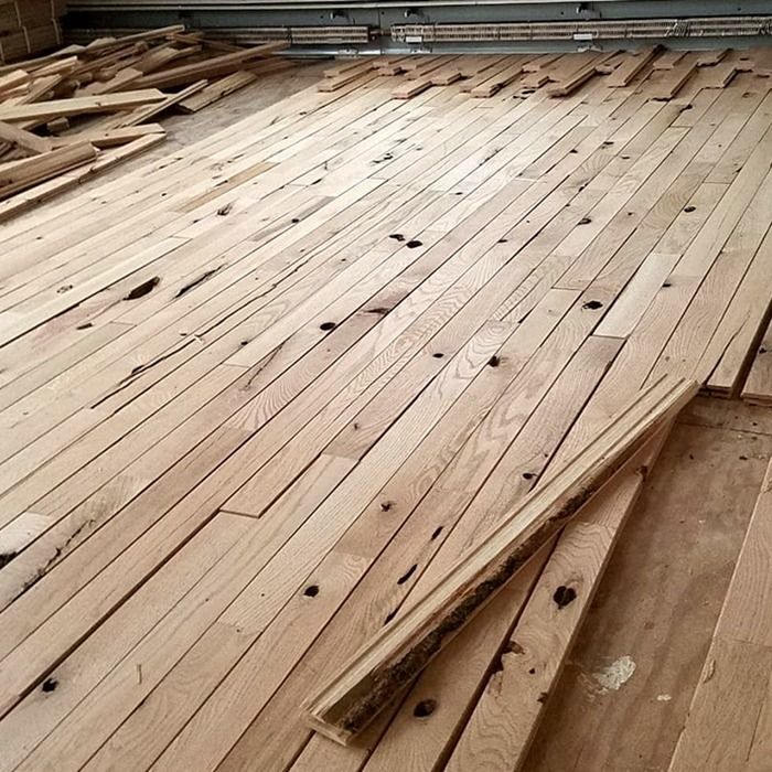 Stacks of unfinished light wood planks laid across a workshop floor with scattered lumber around them