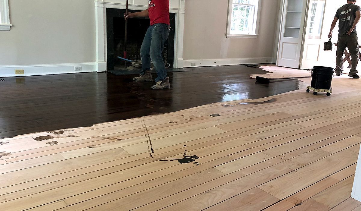 Workers installing dark hardwood flooring in a room, with new light wood planks in the foreground.