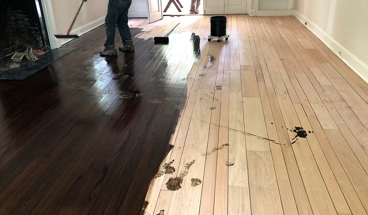 Workers installing dark and light wood flooring in a room, with tools and scattered debris.