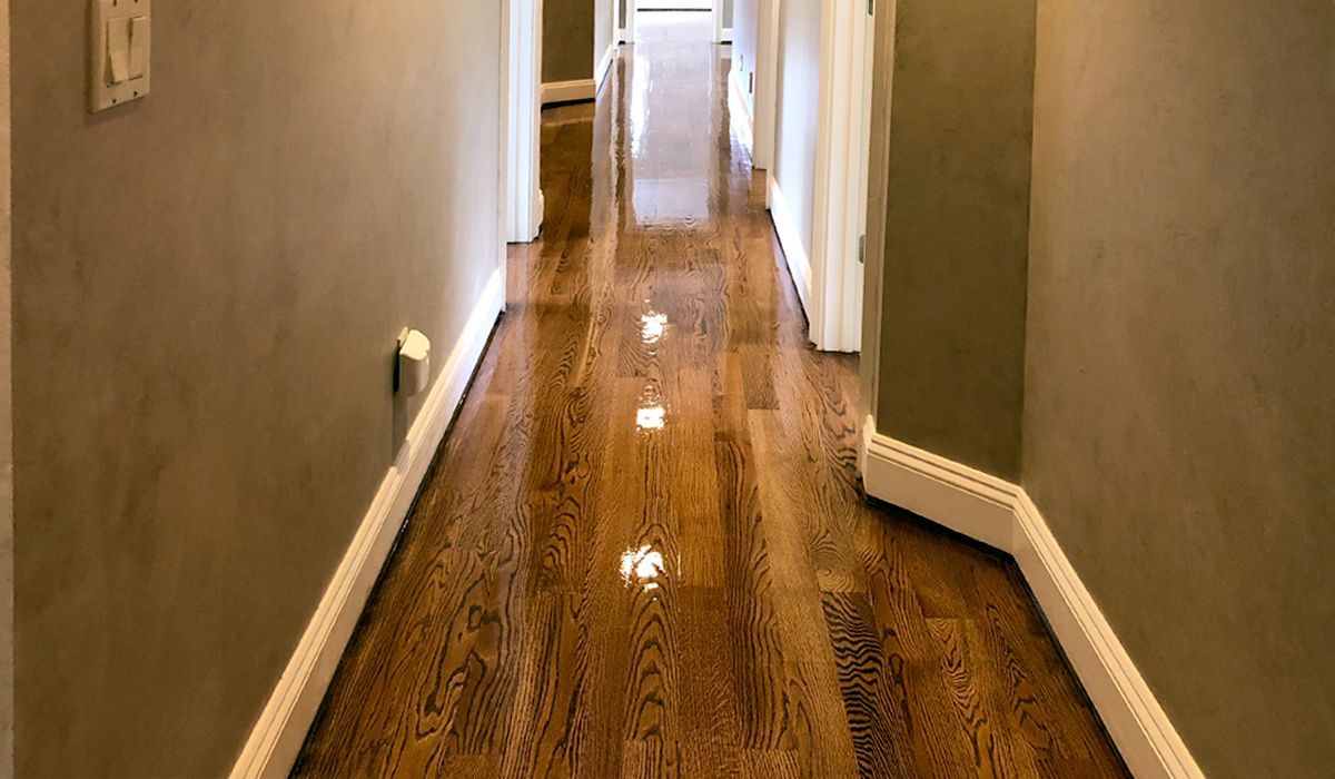 Narrow hallway with polished wooden floor, white trim, and beige walls