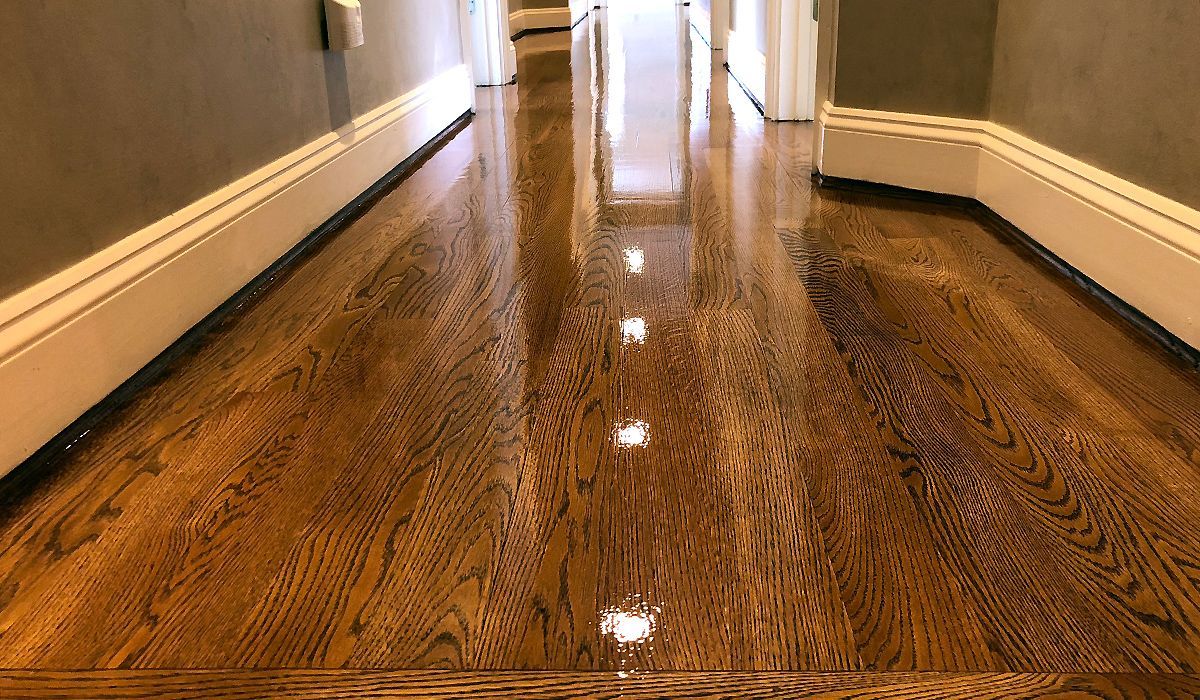 Shiny hardwood hallway floor reflecting light between beige walls and white baseboards