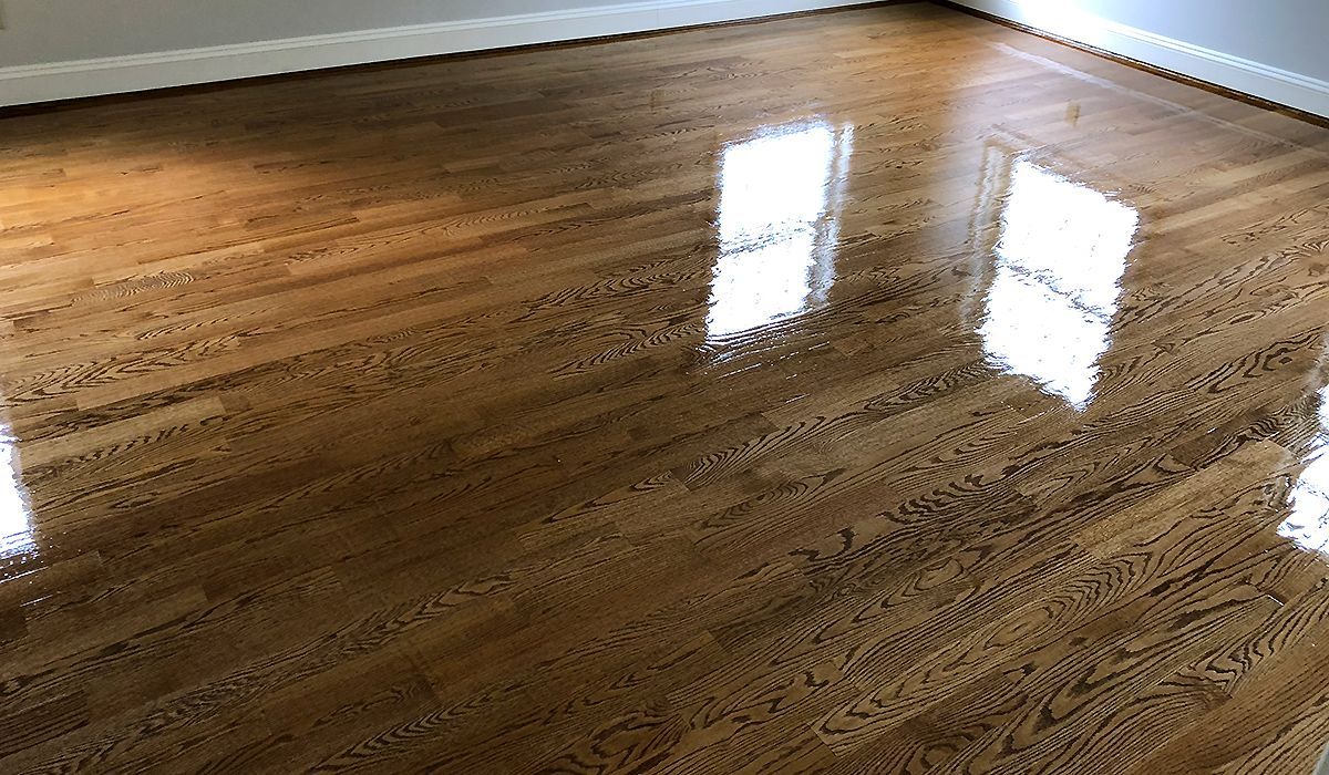 Empty hardwood room with a glossy floor reflecting window light.
