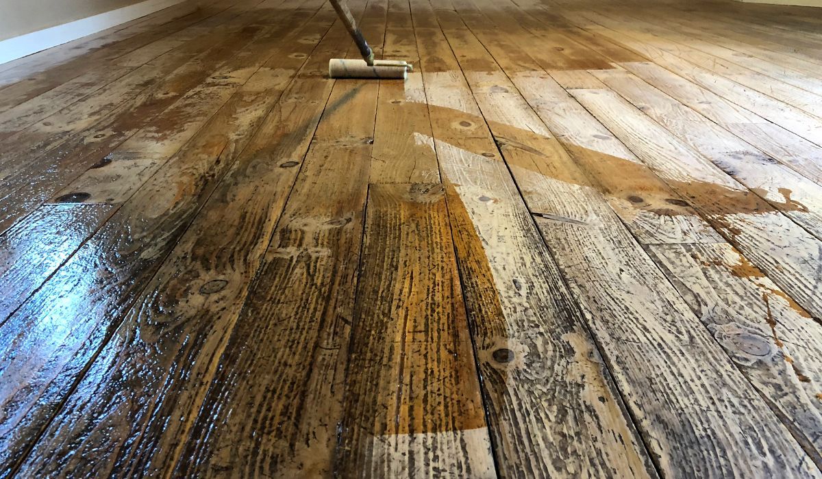 Dirty wooden floorboards being cleaned with a mop, showing wet streaks and scrub marks.