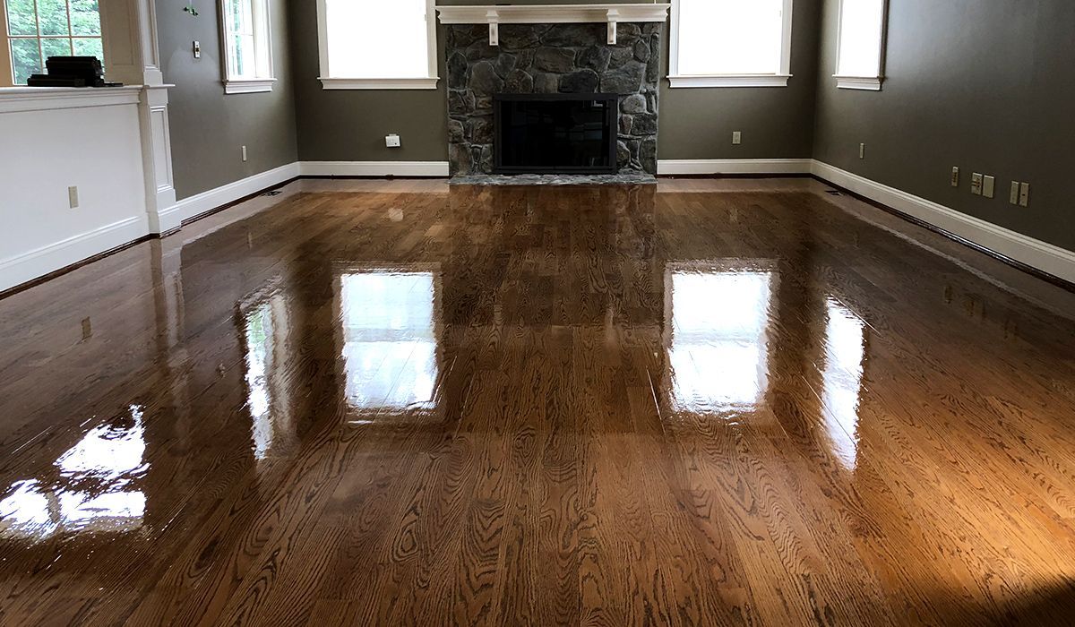 Empty living room with polished hardwood floors and a stone fireplace, reflecting window light.