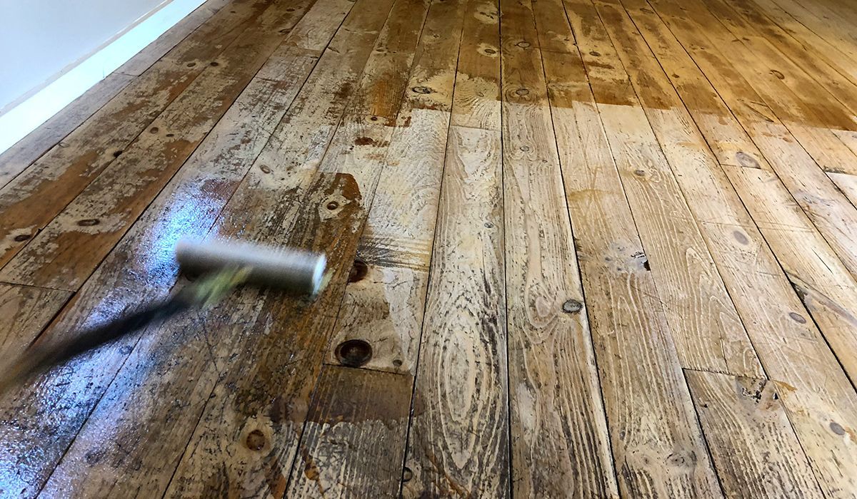 Paint roller on a worn wooden floor, with a paint can in the background.