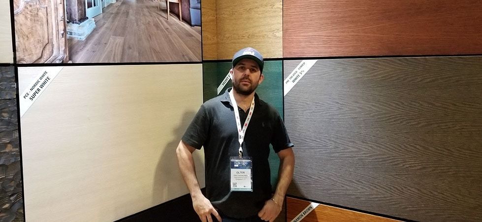 Man standing in front of a beige wall at a conference, wearing a black shirt and lanyard.