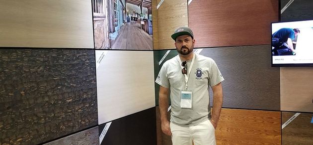 Man in white outfit and cap standing in a modern hallway with textured wall panels and a wall screen.