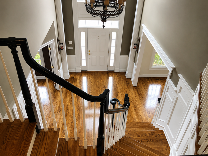 Bright foyer with curved staircase, white doors, and polished wood floors under a chandelier