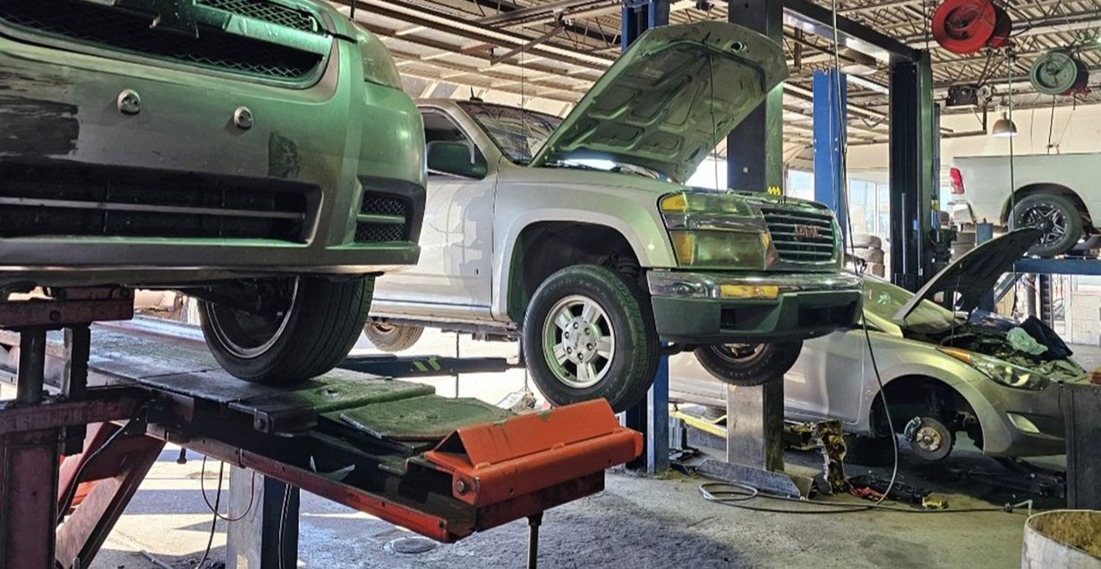 Auto repair shop with several raised vehicles, including a green SUV in front and a silver truck in the center.