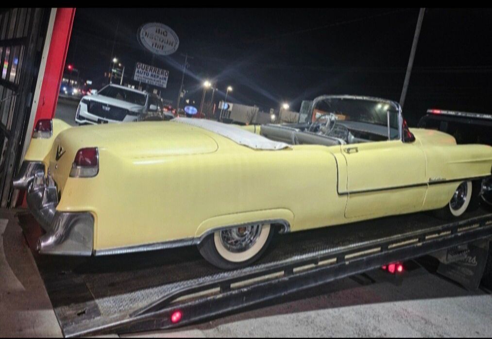 Yellow vintage convertible on a car trailer at night, parked outside a garage.