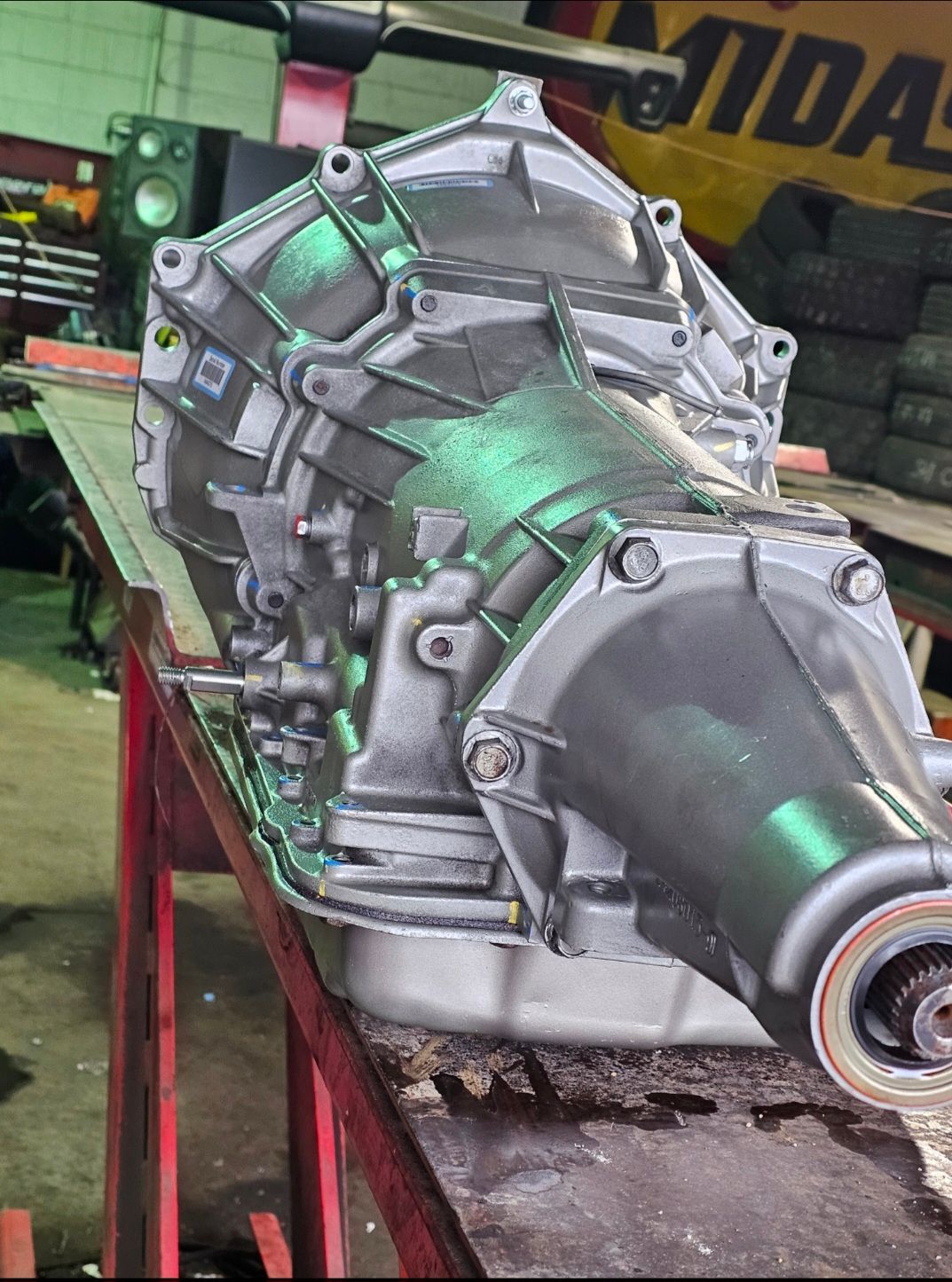 Large metal gearbox on a red stand in a workshop, with green reflections and a visible shaft end.