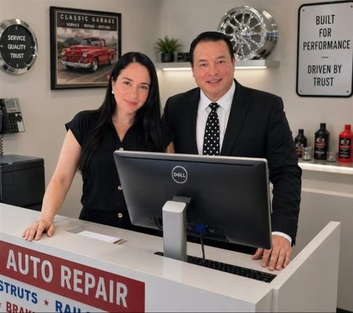 Two people at an auto repair reception desk, standing behind a computer monitor in a shop office.