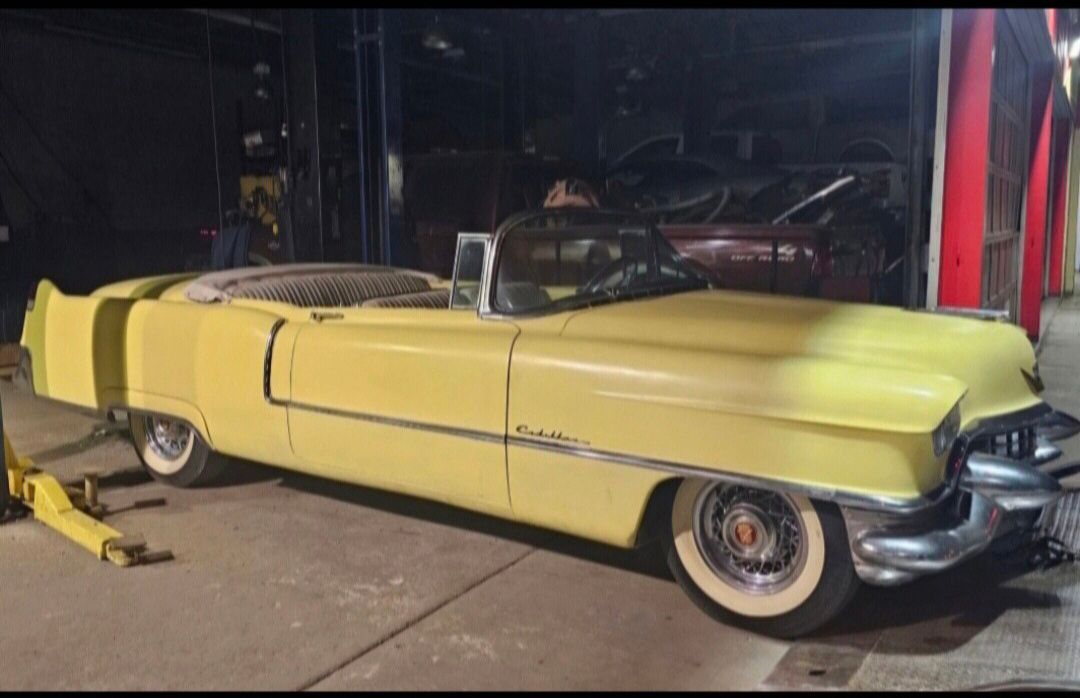 A yellow 1955 Cadillac Series 62 convertible parked inside a garage.